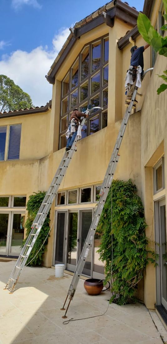 Ladders set against a tall stucco home during a window cleaning job